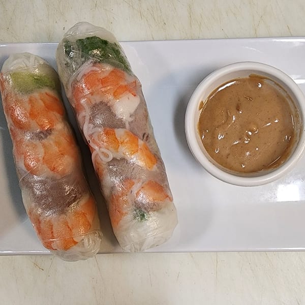 Two fresh Vietnamese spring rolls filled with shrimp and greens, served with a side of peanut sauce.