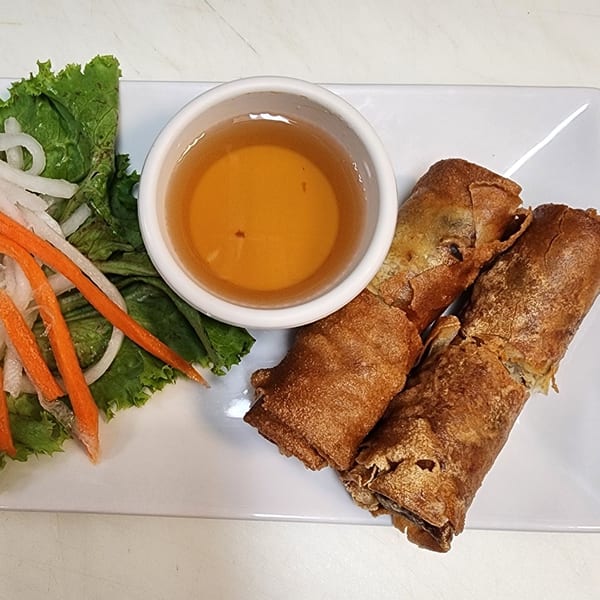 Three crispy Vietnamese egg rolls with a side of lettuce, pickled carrots, daikon, and dipping sauce.