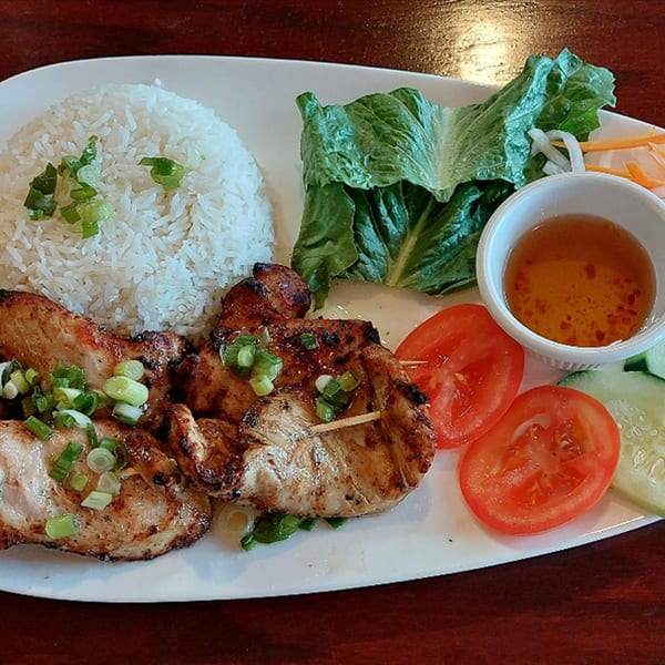 Grilled chicken with rice, lettuce, tomatoes, cucumbers, pickled vegetables, and dipping sauce on a white plate.